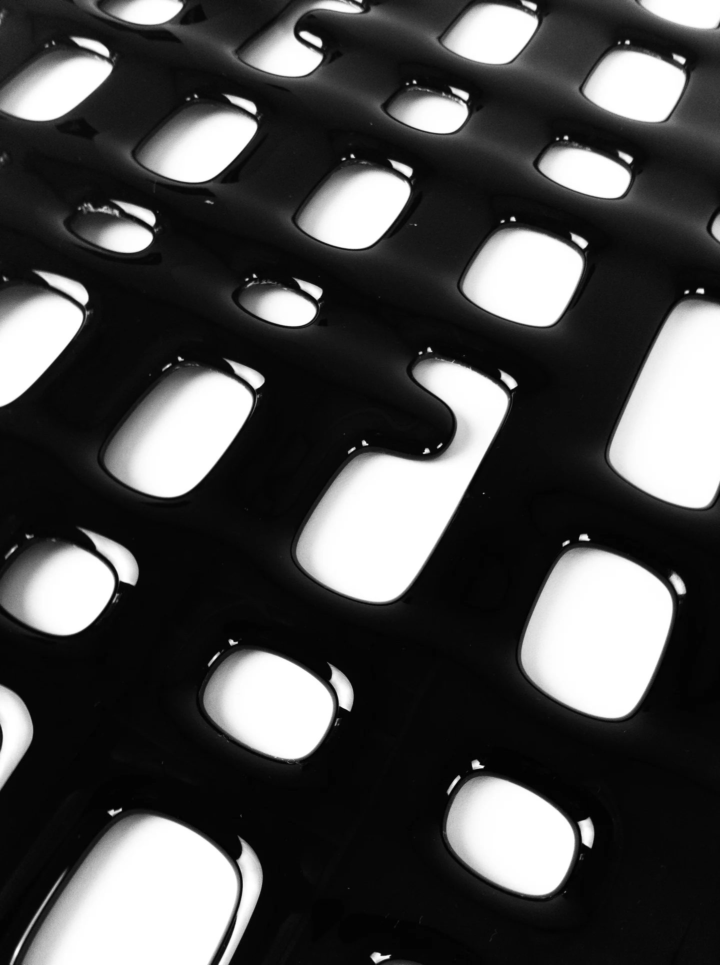 Black-and-white close view of a glossy glass surface with rounded openings