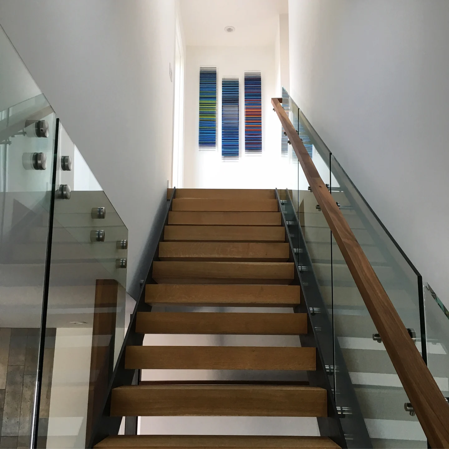 Three narrow, colour-striped glass panels above a wooden staircase with glass balustrades